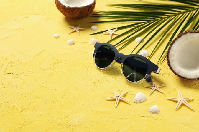 Starfishes, coconut, palm branch and sunglasses on yellow background, space for text