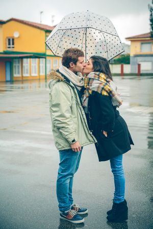 Couple kissing under dotted umbrella on rainy day