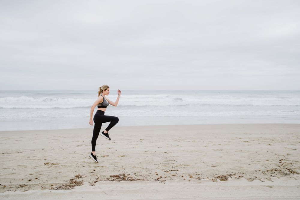 Young female athlete in active wear jogging while jumping at sea beach