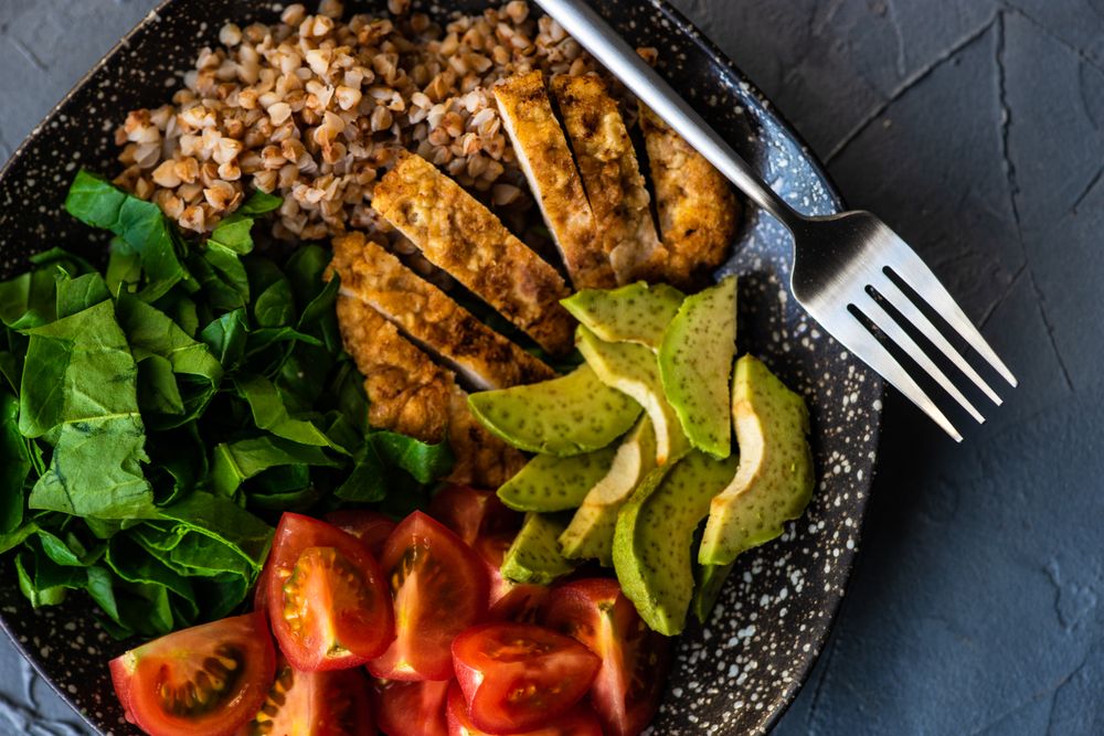 Top view of healthy fresh meal with avocado, grains, tomatoes & spinach