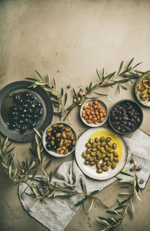 Variety of olives in bowls with branches and linen on concrete background, copy space