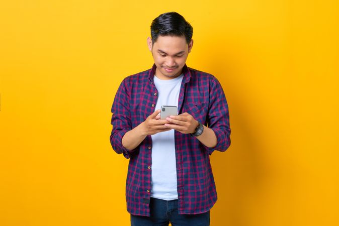 Asian man in plaid shirt  looking down at smartphone