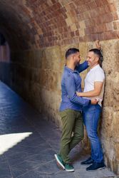 Two men facing each other and embracing under a city bridge, vertical