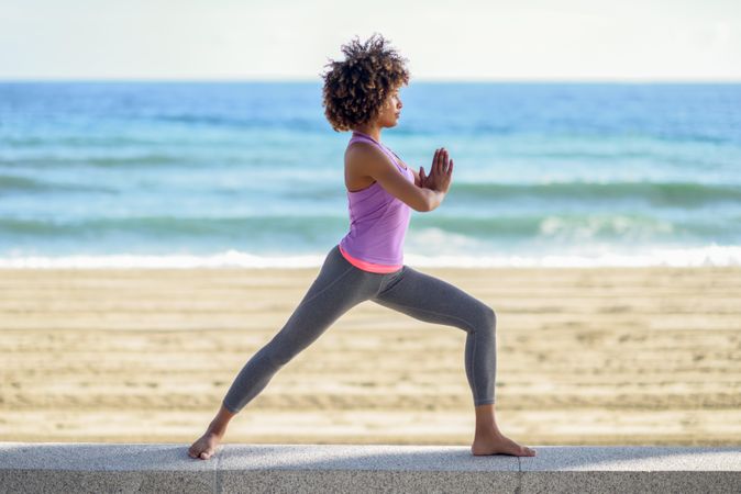 Side view of Black woman with afro hairstyle doing yoga warrior pose near beach