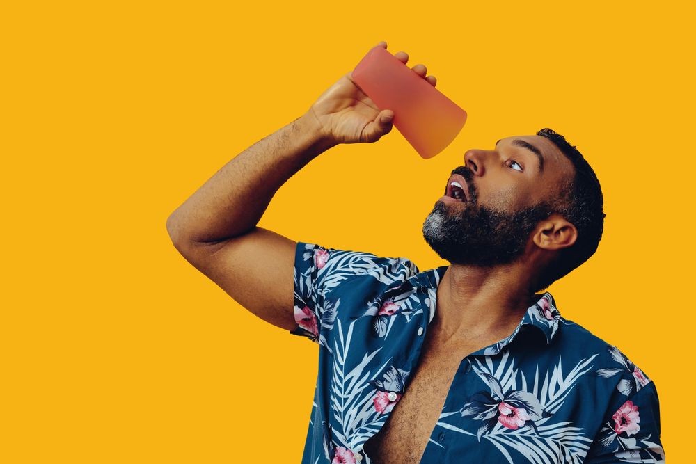 Male chugging a cocktail from orange cup into his mouth in yellow studio