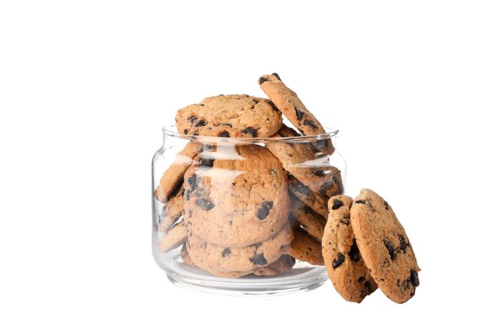 Glass jar with tasty chocolate chip cookies on plain background