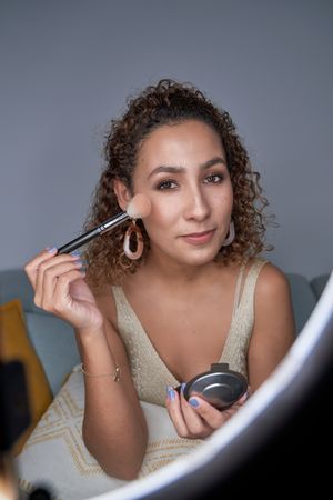 Young positive female blogger demonstrating applying of highligh