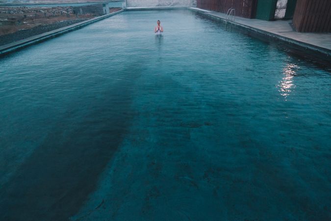 Woman in pool near sea and hills on shore