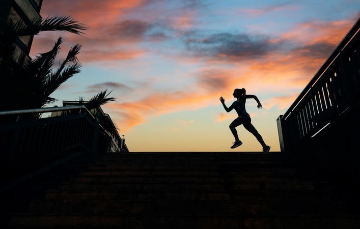Silhouette of female runner working out against a sunset sky