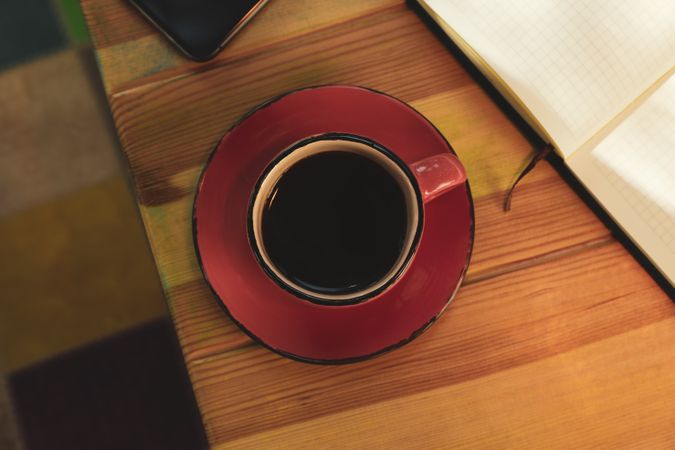 Cup of coffee, notebook and phone on wooden table