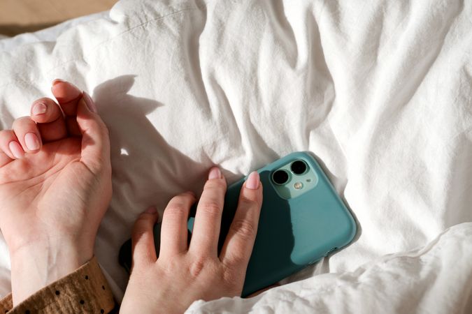 Hand holding smartphone on bed