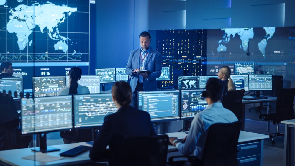 Executive Leads Team in Cutting-edge Data Center. Analysts Monitor Global Information on Multiple Screens.