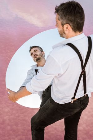 Stylish man holding mirror up and reflecting