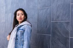 Asian brunette woman with long hair leaning on the wall and looking away