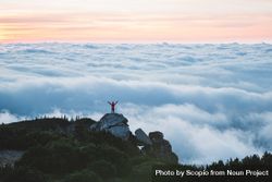 Person standing on rock raising hand on top of the mountain above the clouds 4Aodz0