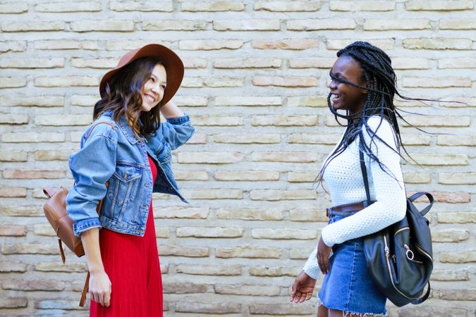 Two women facing each other and talking beside a brick wall
