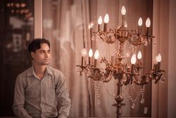 Man in light dress shirt beside brass upplight chandelier