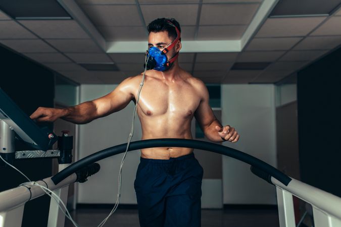 Professional athlete with mask running on treadmill in gym and monitoring his performance
