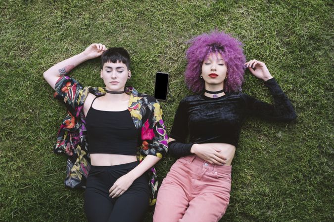 Women in colorful shirt and with pink hair lying on grass