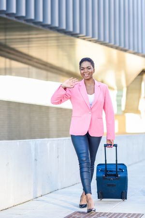 Happy Black woman with travel bag wearing pink jacket walking outside