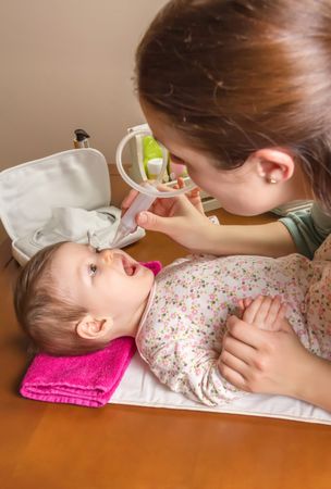 Baby entertained by nasal aspirator with mother