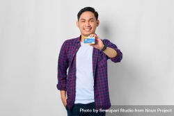 Asian male in grey studio holding up credit card 0PeZr5