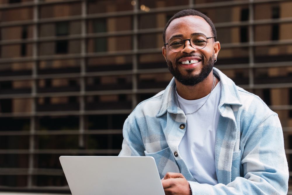 Cheerful Black man browsing laptop on street