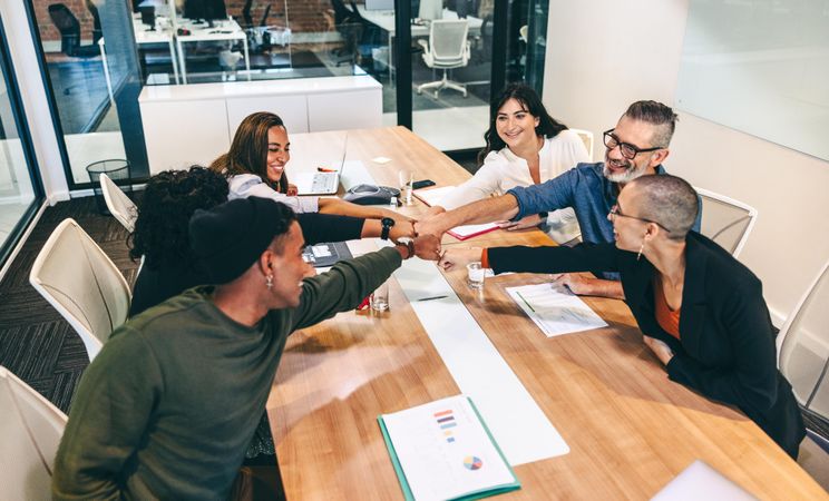Group of happy businesspeople bringing their fists together while sitting in a boardroom