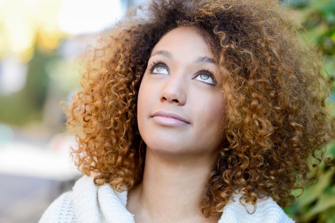 Woman with curly hair standing outside looking up