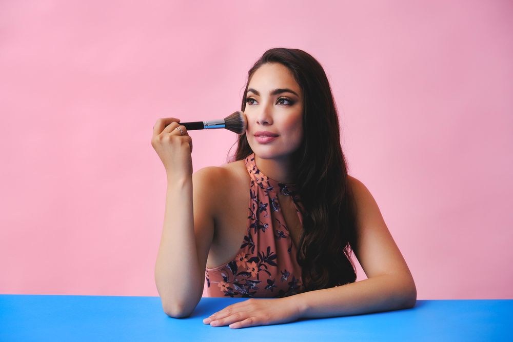 Hispanic woman with long brown hair holding large make up brush