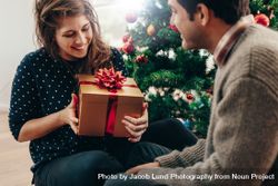 Smiling couple exchanging Christmas gifts in their living room 0KMVDy