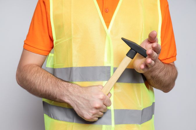 Engineer with hammer in hands on gray background, close up