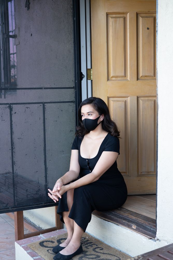 Woman sitting by front door of house with mask