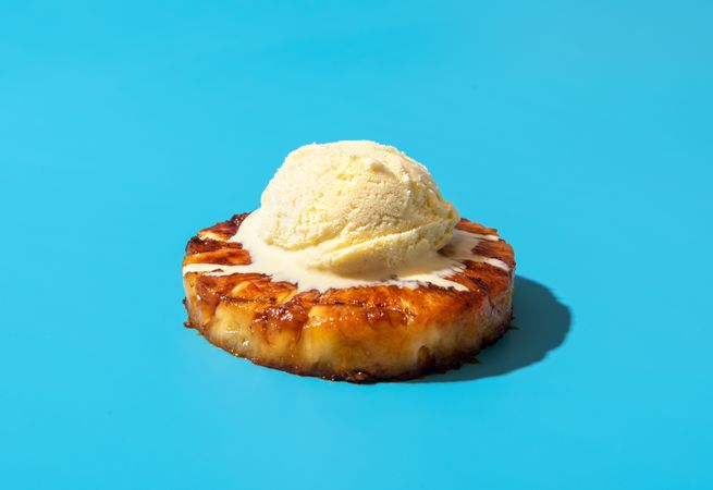 Grilled pineapple with vanilla ice cream, isolated on a blue background