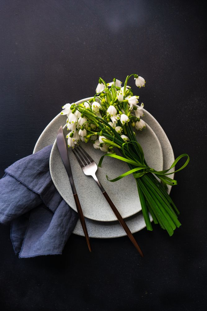Top view of table setting for spring dinner with flowers on grey plate with space for text