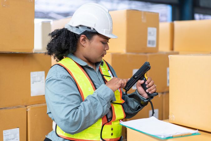Woman in safety gear working in warehouse checking bar codes on stock