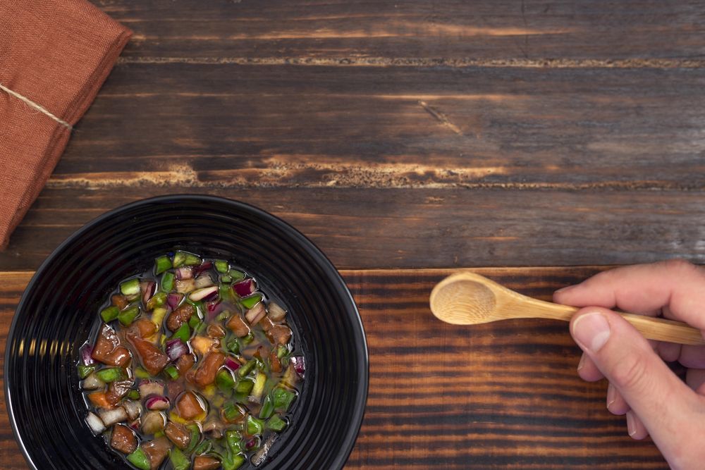 Person holding wooden spoon and a bowl of vegetable soup on table