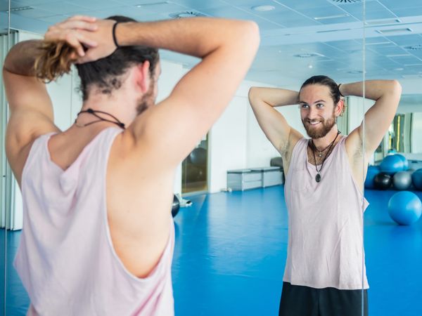 Smiling man looking at mirror in fitness room