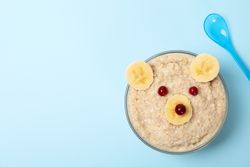 Bear face made of porridge and fruits on blue background, top view. Baby food