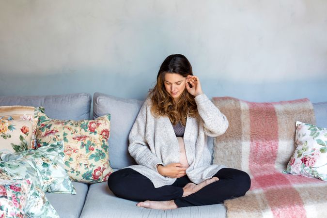 Relaxed pregnant woman lounging at home sitting cross legged on sofa