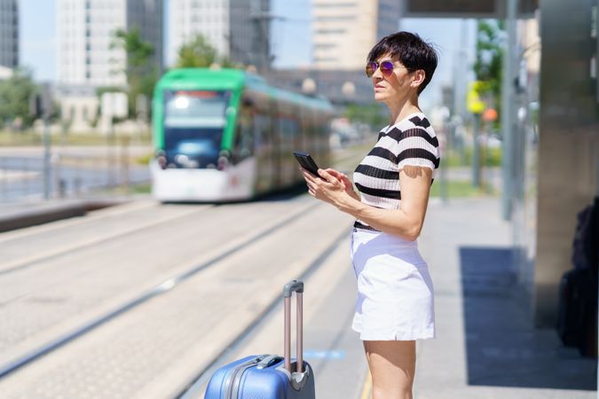 Woman checking phone while waiting for train with large suitcase