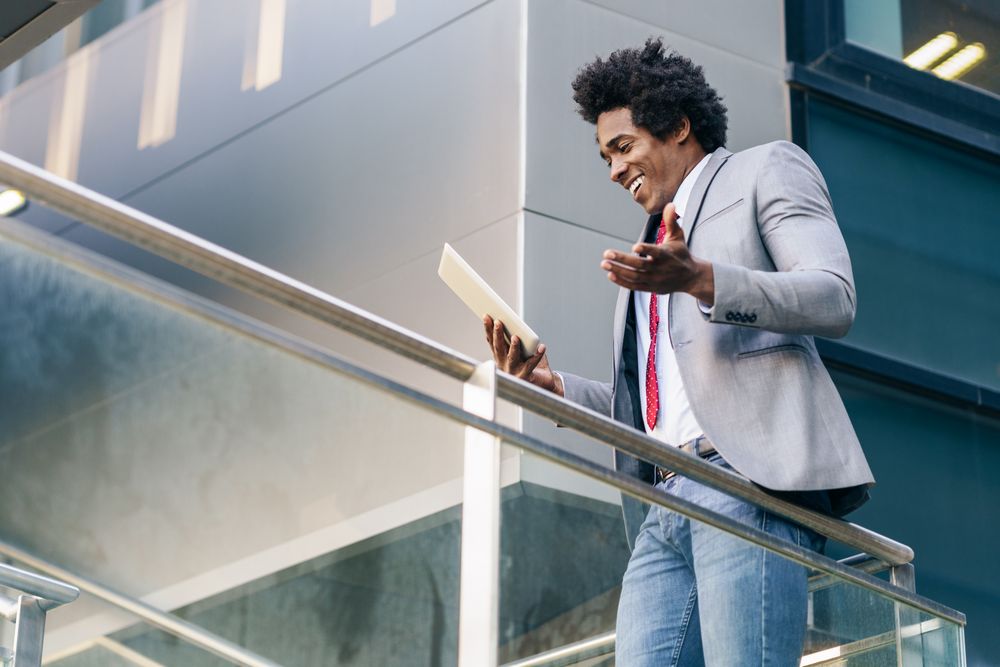 Smiling man speaking at his digital tablet while walking up staircase