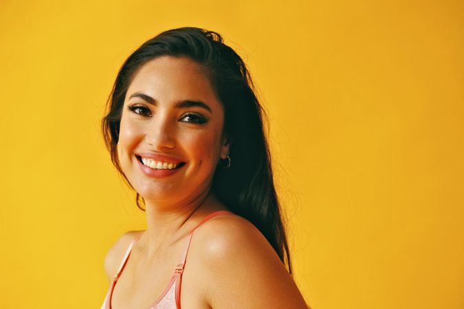 Headshot of smiling confident Hispanic woman standing in front of a yellow background