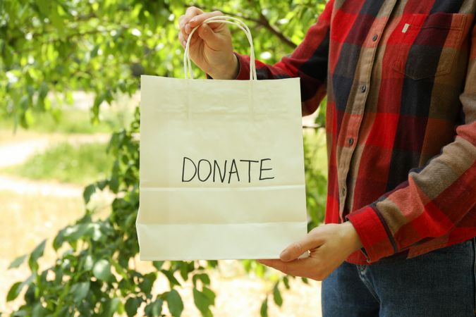 Woman holding paper bag with text Donate outdoor