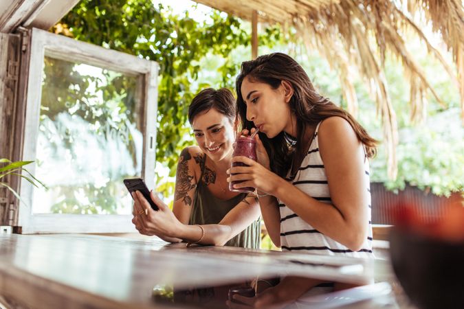 Two happy women sitting at a restaurant looking at mobile phone