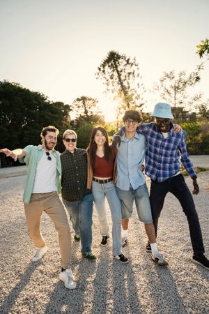 Full length vertical shot of diverse friends walking together outdoors at sunset.
