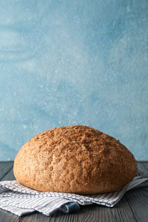 Bread on kitchen towel on wooden table against light background, space for text