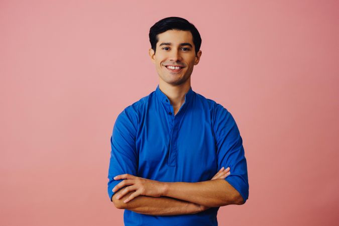 Medium shot of smiling Latino man in pink studio with arms folded