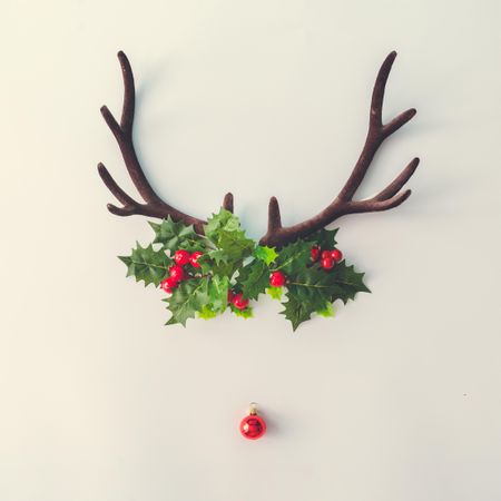 Brown antlers making reindeer face with holly and bauble on light background