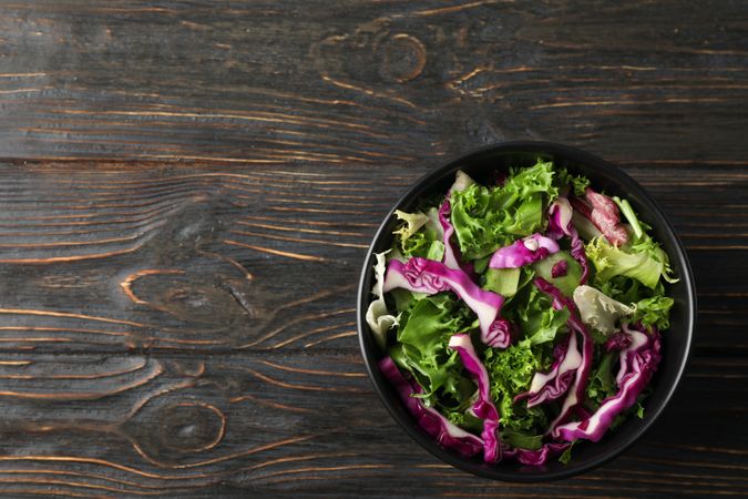 bowl with fresh vegetable slices on wooden background, top view
